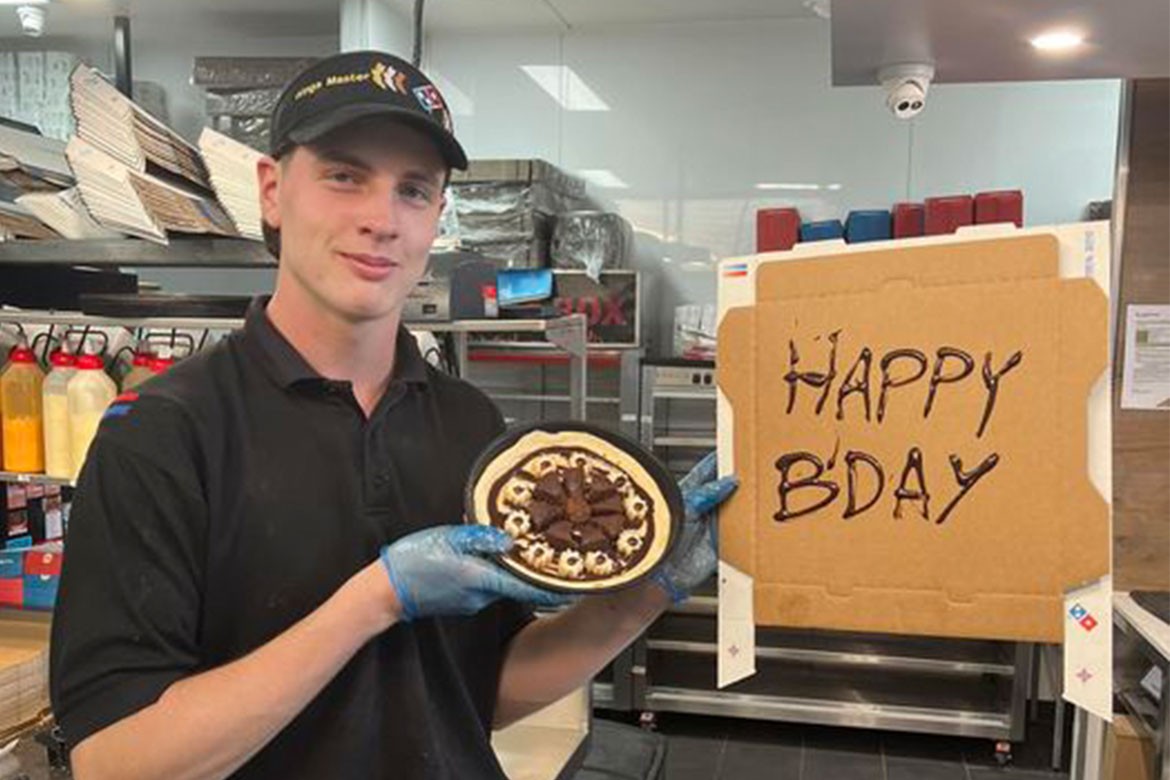 Miles (Domino's Coolum manager) stands in a shop holding a dessert pizza and a pizza box with 'happy birthday' written on it in chocolate sauce (Domino's Coolum)