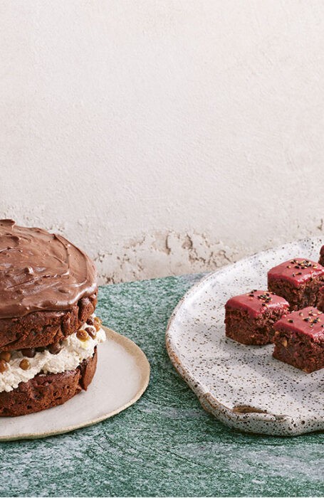 A delicious looking beetroot, chocolate, and wattleseed cake sits next to a plate full of mini-cakes