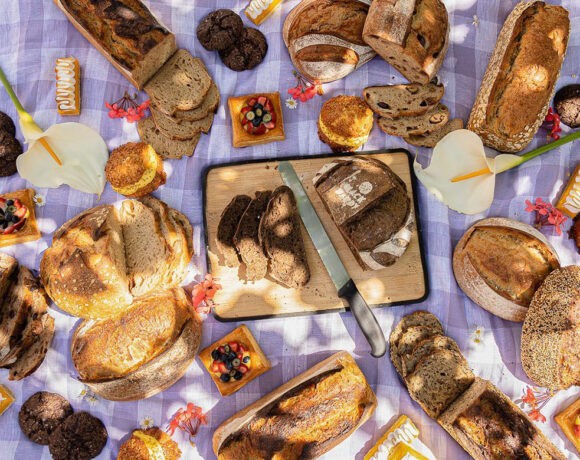 A picnic spread of various loaves of bread, positioned beautifully around a large loaf of bread in the middle of the picnic rug on a chopping board (Back Alley Bakes)
