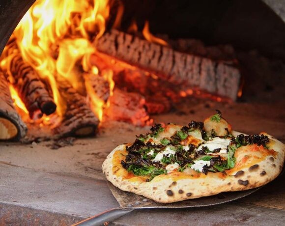 A wood-fired pizza being taken out of the oven on a metal pizza pallette (2023 trends)