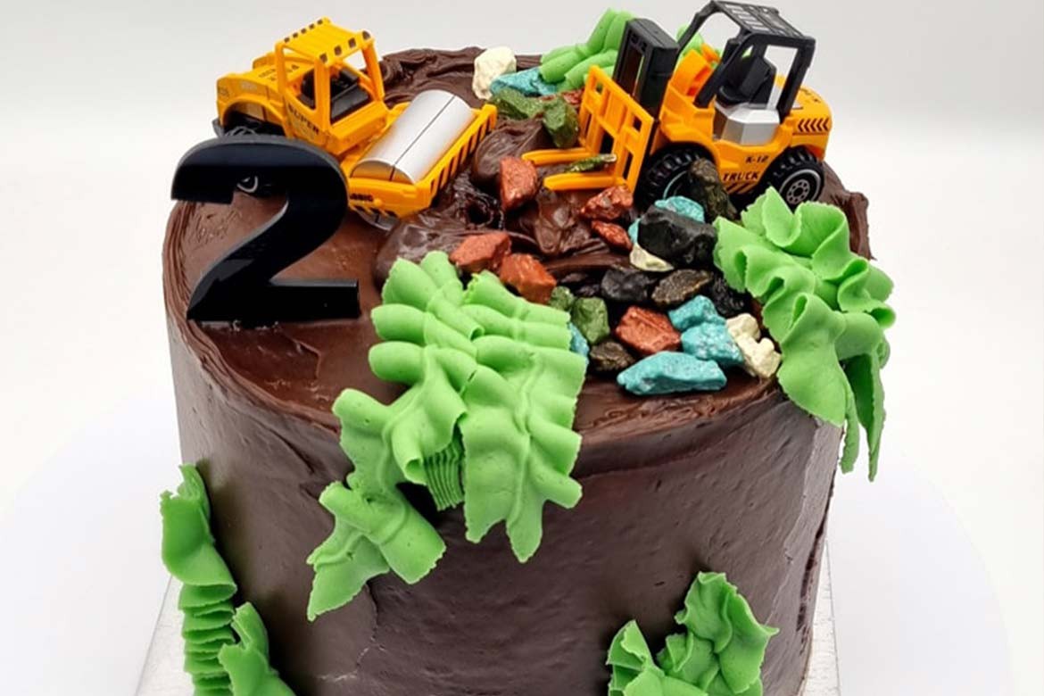A cake covered in chocolate icing decorated with heavy building equipment toys and icing leaves (Sarah's Cakes)