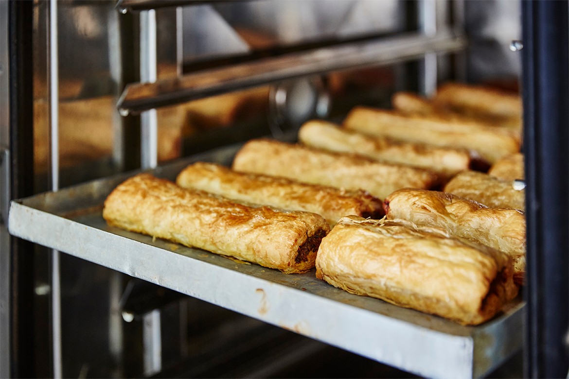 Lifestyle reportage photography of a pie and pastry wholesale bakery factory, sausage rolls that have finished baking in industrial oven (South Australian Baking Show 2023)