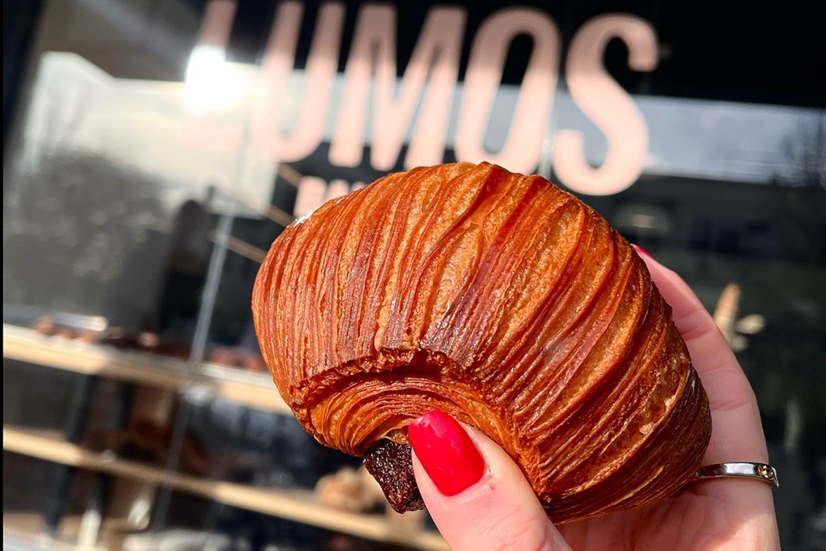 a woman's hand holds a brownie croissant in front of the Lumos shopfront window