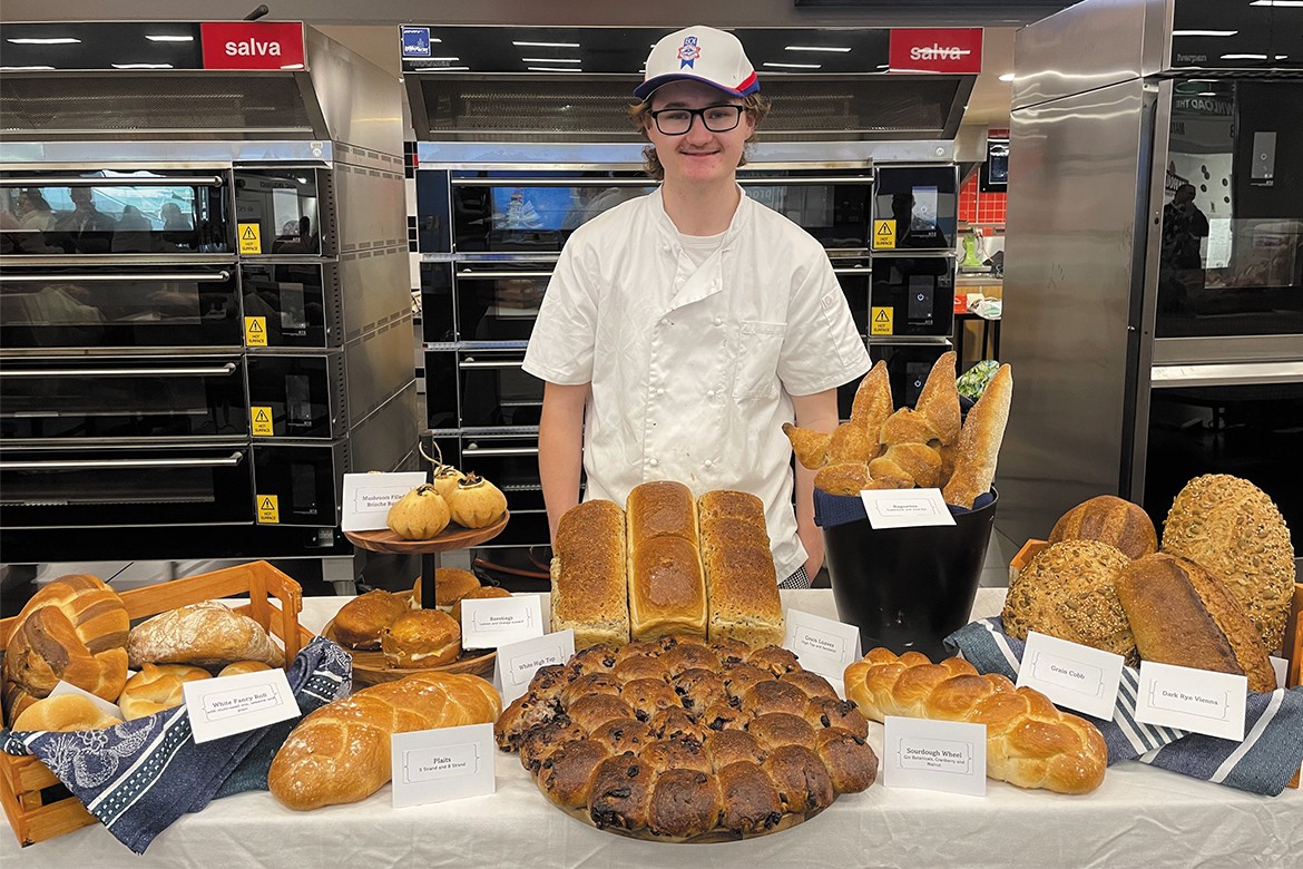 Caleb Braszell standing behind a table full of bread (Excellence in Baking)