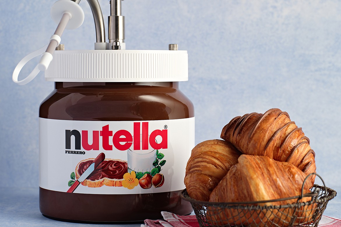 Nutella dispenser sitting next to a small metal basket full of croissants
