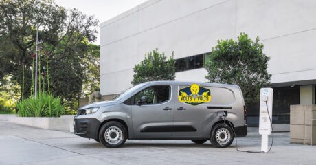 the Peugeot e-Partner Van is parked in front of a commercial building, plugged into an electric vehicle charger