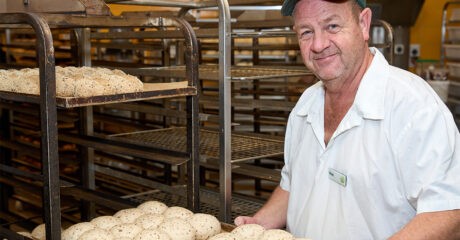 Nicol Strang holding a tray of unbaked bread rolls in the Woolworths kitchen