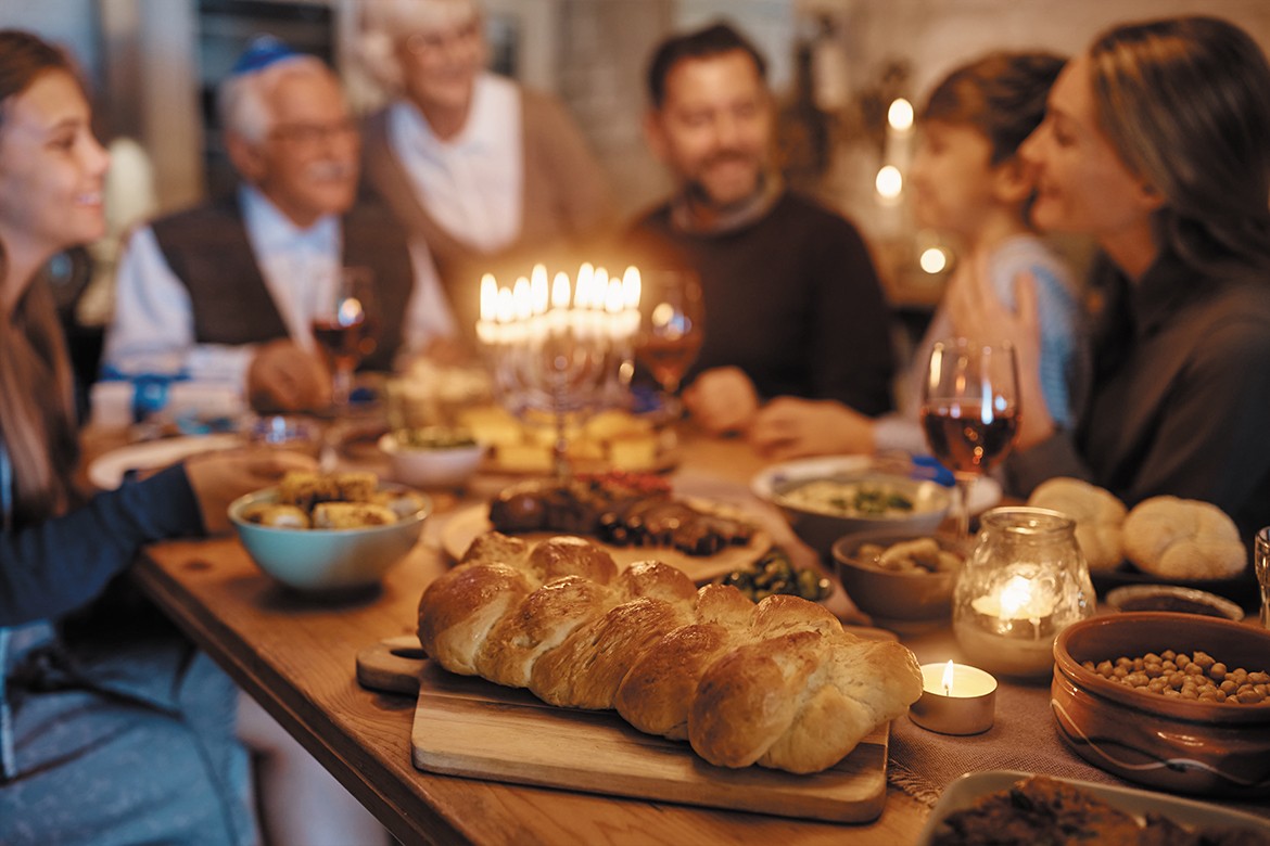 Challah bread on dining table with extended Jewish family in the background (Hanukkah)