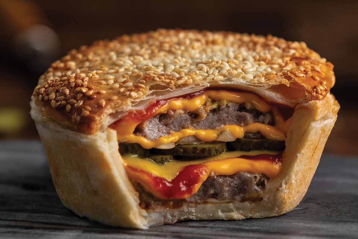 Banjo's Bakery Cafe will be opening on the Gold Coast. Oictured is the brand's double cheeseburger pie, cut open so you can see the filling. It sits on a wooden table.