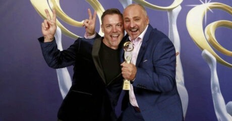 OMG Donuts directors are pitcured holding their golden trophy standing in front of a purple and gold background. Both men are giving the peace sign after winning at the 2024 Australian Small Business Champion Awards.