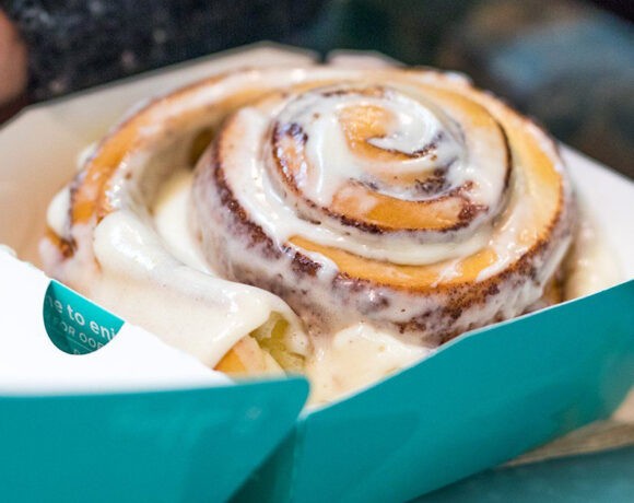 Cinnabon scroll glaazed with white icing sits in a blue box with a white interior.