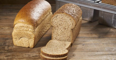 Wholemeal bread sits sliced on a wooden counter.
